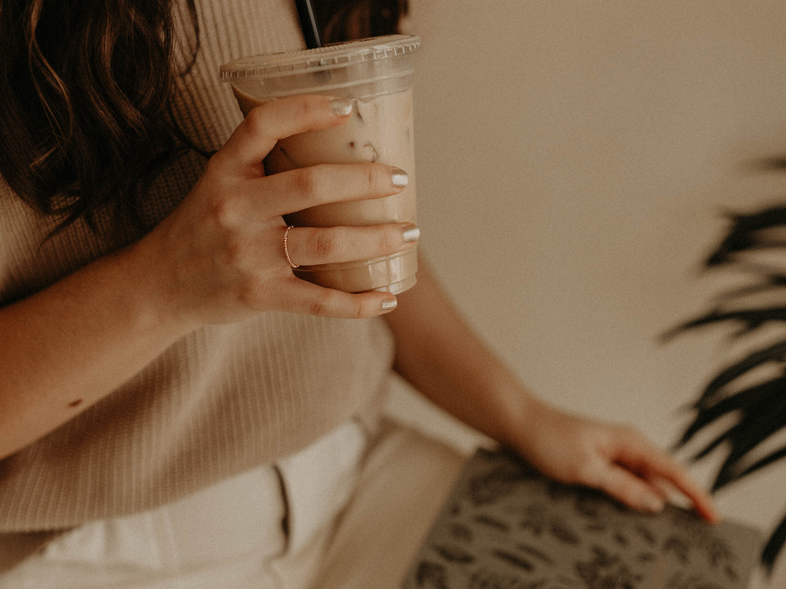 A woman is drinking an iced coffee and holding a green notebook.